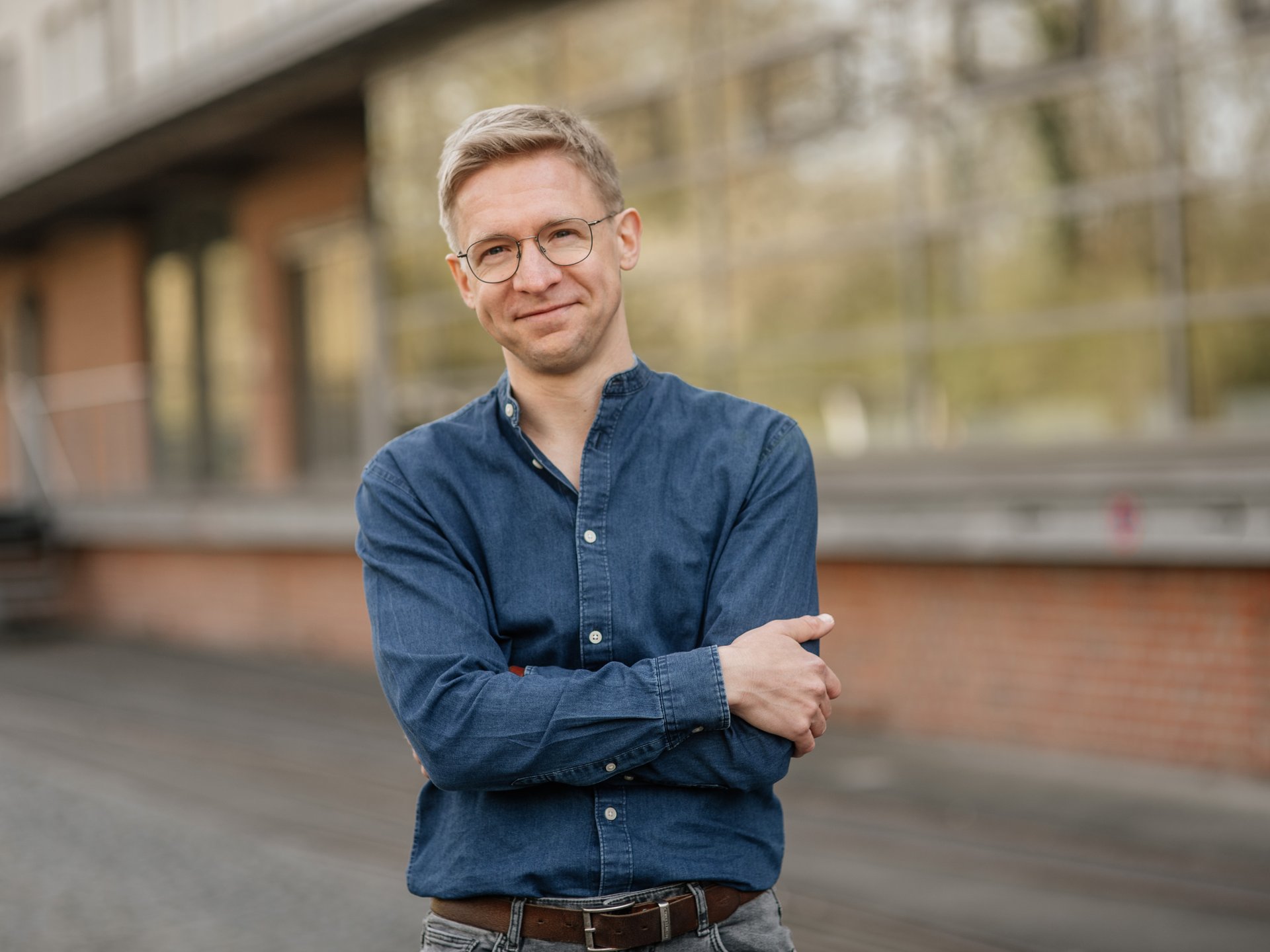 Ein Mann steht auf einer Straße und verschränkt lächelnd die Arme